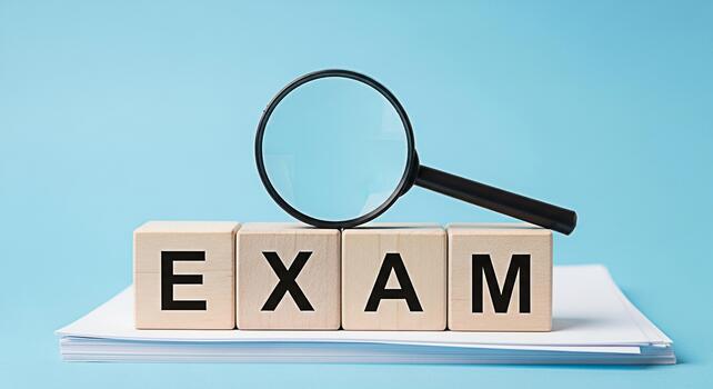 Magnifying glass inspecting the word EXAM spelled out with wooden blocks on a stack of papers against a blue background representing scrutiny and the importance of preparation photo