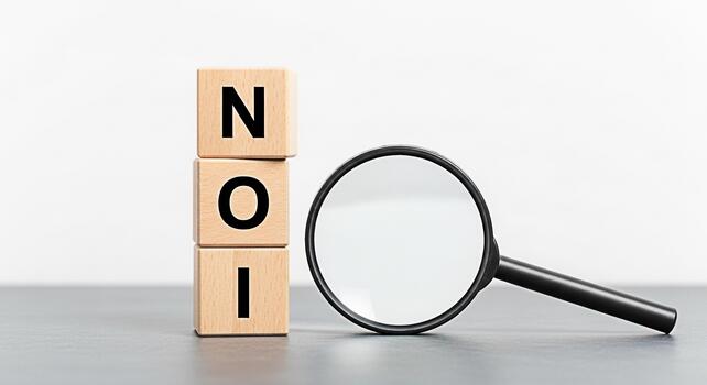 Magnifying glass examining wooden blocks spelling NOI on a gray table against a white background representing net operating income analysis and financial investigation with a focus on profitability an photo