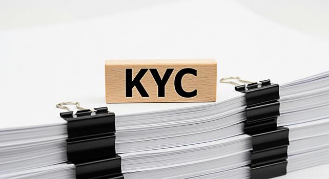 KYC wooden block resting on a stack of documents secured with binder clips in a bright minimalist office setting representing compliance verification and regulatory adherence for financial institution photo