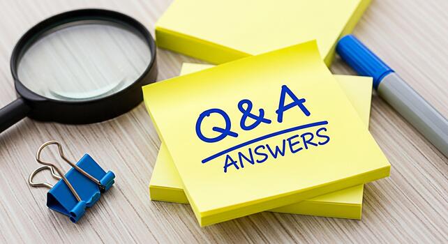 Closeup of yellow sticky notes displaying QA Answers on a wooden desk accompanied by a magnifying glass paper clip and pen symbolizing clarity information and problemsolving in a professional setting photo