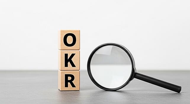 Wooden blocks displaying OKR acronym next to a magnifying glass on a gray surface representing objectives and key results in a business setting symbolizing focus clarity and strategic planning photo