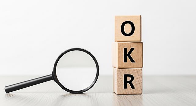 Magnifying glass inspecting wooden blocks spelling OKR on a bright wooden surface symbolizing objectives and key results with a focus on business goals and performance measurement in a corporate setti photo