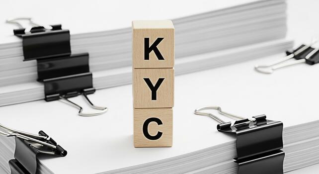 Wooden blocks displaying KYC acronym amidst stacks of documents and binder clips on a white surface representing compliance identity verification and regulatory requirements in a business setting photo