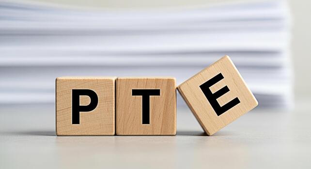 Wooden blocks spelling PTE on a bright desk with a stack of papers in the background representing the Pearson Test of English and the concept of language proficiency and academic success photo