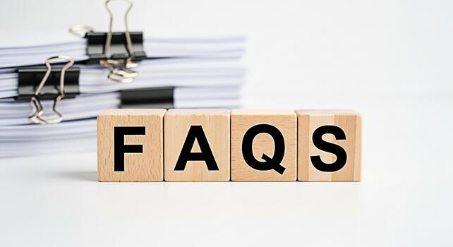 Wooden blocks spelling FAQs on a white surface with a stack of documents in the background representing information access and customer service in a clean and professional setting photo