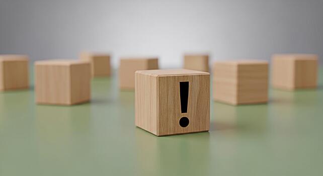 Wooden block displaying an exclamation point on a green surface surrounded by other blocks symbolizing urgency and attention to detail in a minimalist and clean environment photo