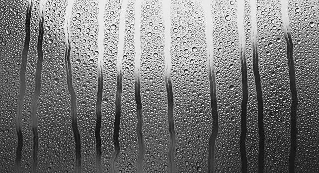 Condensation droplets clinging to a window pane forming rivulets and patterns in a steamy environment evoking a sense of introspection and the beauty of transient natural phenomena photo