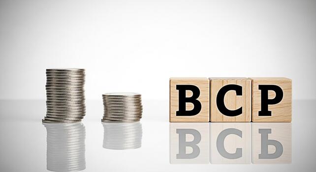Stacks of coins beside wooden blocks spelling BCP on a reflective surface representing Business Continuity Planning in a financial context emphasizing preparedness and risk management photo