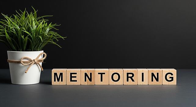 Wooden blocks spelling MENTORING on a dark surface with a potted plant symbolizing guidance and support in a professional environment fostering growth and development with a positive and encouraging m photo