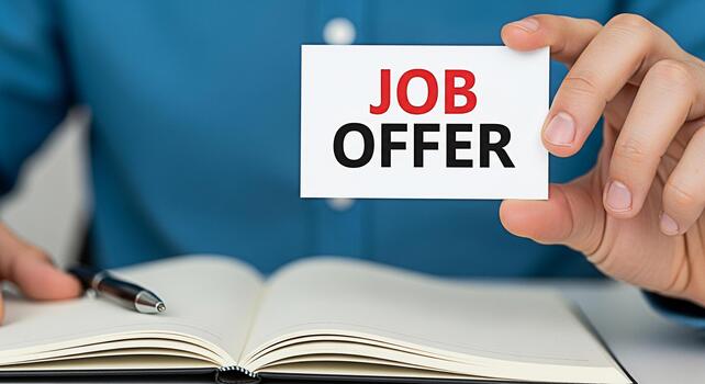 Person holding a job offer card in front of an open notebook with a pen symbolizing new career opportunities and a promising future in a professional and optimistic setting photo
