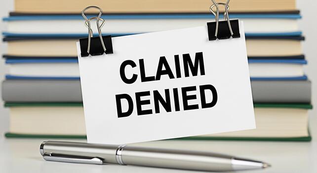 Formal notification of a denied claim displayed on a white card with binder clips resting on a desk with a pen and stack of books conveying a sense of rejection and financial setback photo