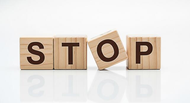 Wooden blocks spelling STOP on a white reflective surface conveying a message of caution and prevention in a clean minimalist environment symbolizing control and the need to halt unwanted actions photo