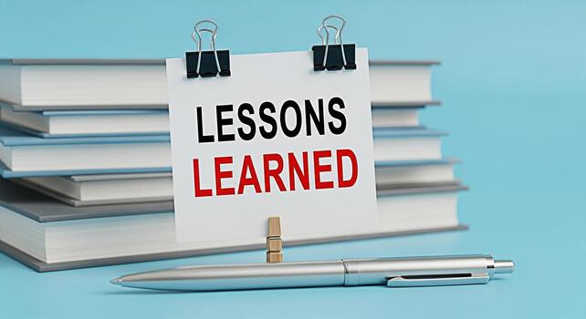 Lessons Learned message displayed on a white card held by binder clips stacked books in the background with a pen lying on a blue surface symbolizing education and experience photo