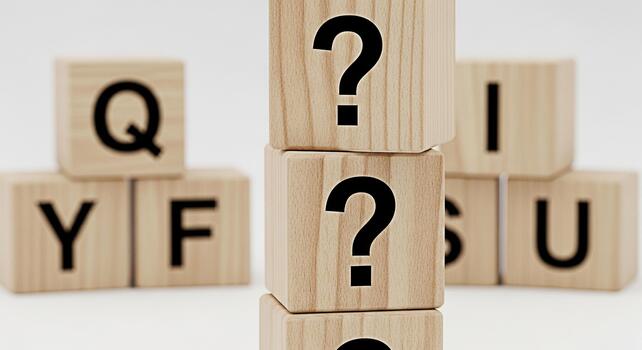 Stacked wooden blocks displaying question marks and random letters on a white surface representing uncertainty and the search for answers in a minimalist and conceptual composition photo