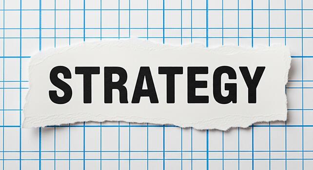 Bold Strategy text displayed on a torn piece of paper placed on a blue grid background conveying a message of planning and direction for business success and effective decisionmaking photo