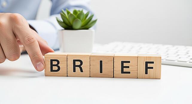 Hand arranging wooden blocks spelling BRIEF on a white desk with a succulent plant and keyboard symbolizing concise communication and efficient planning in a modern office environment photo