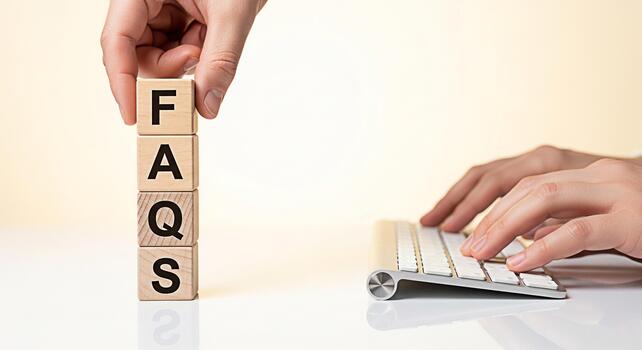 Human hand stacking wooden blocks spelling FAQs next to a keyboard on a white desk representing frequently asked questions and customer support in a modern and minimalist office environment photo
