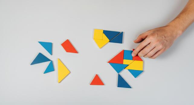 Hand arranging colorful geometric puzzle pieces on table for problem-solving activity photo