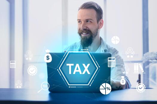 Man smiling while working on laptop with tax graphics and icons in a modern office setting photo