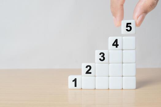 Close-up of a man's hand placing the fifth dice on a staircase-like stack on a wooden table, symbolizing growth, progress, or step-by-step success photo