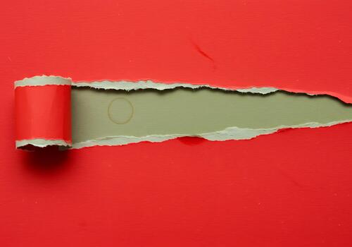 A vivid red paper sheet dramatically torn horizontally exposing a muted green background underneath with a textured rolled edge photo