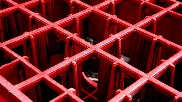 Close-Up of Red Plastic Grid Structure. This image captures a detailed close-up view of a red plastic grid with intersecting square compartments and textured surfaces. photo