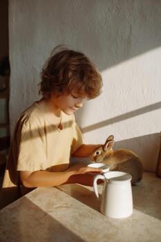 Child gently feeding a pet rabbit in a sunlit room, showcasing a minimalist setting with soft textures and warm ambiance, creating a serene moment of connection photo