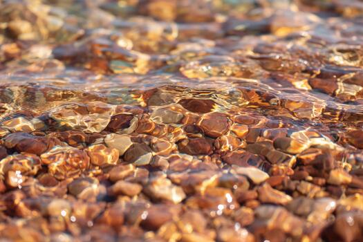 Light reflections dance on the surface of clear water over smooth pebbles, creating a mesmerizing interplay of colors and textures in a tranquil natural setting photo