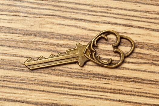Old brass key resting on a wooden table background with visible grain patterns photo