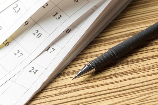 Close-up of a pen resting next to a calendar with various dates highlighted photo