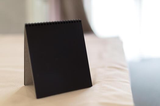 Simple black notepad standing on a white table near a window with soft light photo