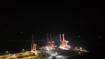 Brightly illuminated cranes unloading a large container ship docked at the commercial port of mersin, turkey, showcasing nighttime industrial activity and global logistic operations video