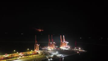 imponerande antenn se av en stor behållare fartyg manövrering till docka på de ljust upplyst mersin internationell hamn terminal, med brygga kranar redo för frakt avlastning video