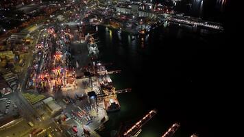 Night aerial view of a bustling industrial seaport with illuminated cranes loading and unloading colorful containers from large cargo ships at the busy terminal video