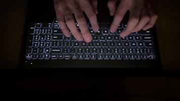 une Haut vue de une homme mains plus de une portable clavier. une fermer de une homme mains dactylographie dans le foncé sur une rétro-éclairé clavier. video
