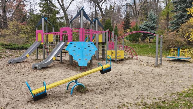 Colorful playground with slides, seesaws, and climbing structures in a park surrounded by autumn trees, creating a cheerful and vibrant outdoor scene for children photo