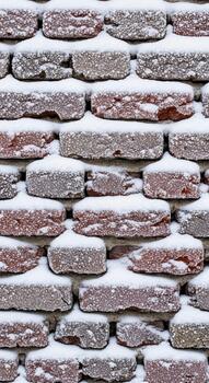 Close up of weathered brick wall covered in a soft blanket of fresh winter snow creating a textured and serene pattern photo