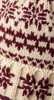 Close up of a cream colored knitted fabric featuring a repeating pattern of maroon snowflake motifs and horizontal stripes photo