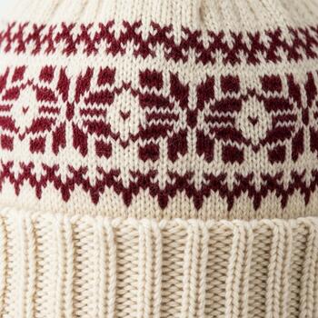 Close up view of a cream colored knitted fabric featuring a repeating pattern of burgundy snowflakes and geometric designs photo