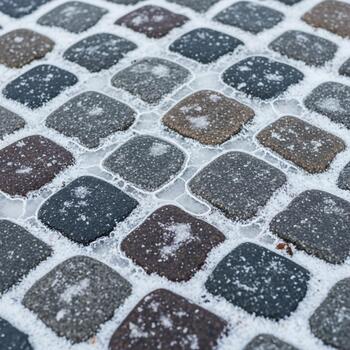 Close up view of weathered cobblestone pavement with a dusting of snow creating a textured winter ground surface photo