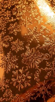 Intricate snowflake patterns embossed on a warm copper or bronze metallic surface with subtle lighting photo