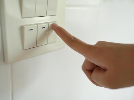 Hand pressing light switch white wall, demonstrating action of turning or off light. image captures moment of interaction with home electrical fixtures, emphasizing functionality and simplicity photo