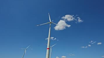 en stor vind turbin mot en blå himmel. väderkvarnar generera energi när de är vände sig förbi de vind medan stående i en fält. de turbin har tre blad den där är bifogad till en Pol video