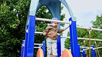 liten 2 år gammal pojke diabilder ner en glida på en lekplats. de pojke har roligt och spelar på en lekplats utanför. de barn är i en jacka och byxor video