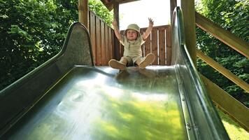 energisk pojke spelar på en lekplats och diabilder ner en hal glida. en barn diabilder ner en hög glida. barns gunga utomhus. video