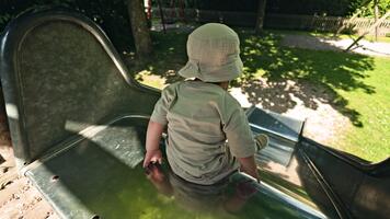 ett energisk pojke spelar på en lekplats och diabilder ner en hal glida. en barn diabilder ner en hög glida. barns gunga utomhus. video