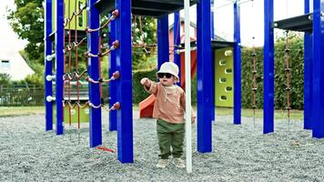 allegro bambino piccolo nel occhiali da sole giocando su terreno di gioco bambino nel Panama cappello su testa in esecuzione su terreno di gioco nel città parco. bambino esplorando ambiente. bambino giocando indipendentemente su terreno di gioco. video