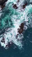 Waves crash against rocky shores creating a vibrant dance of turquoise and white under the sunlight at midday video