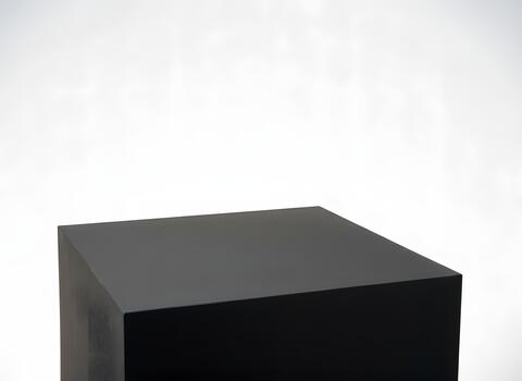 A black cube podium sits in the lower portion of the frame against a bright white background, creating a minimalist and stark composition photo