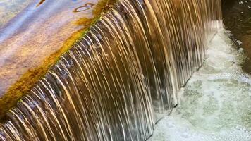 Beautiful cascade of water flowing over a moss-covered ledge in a serene natural setting during a sunny afternoon video